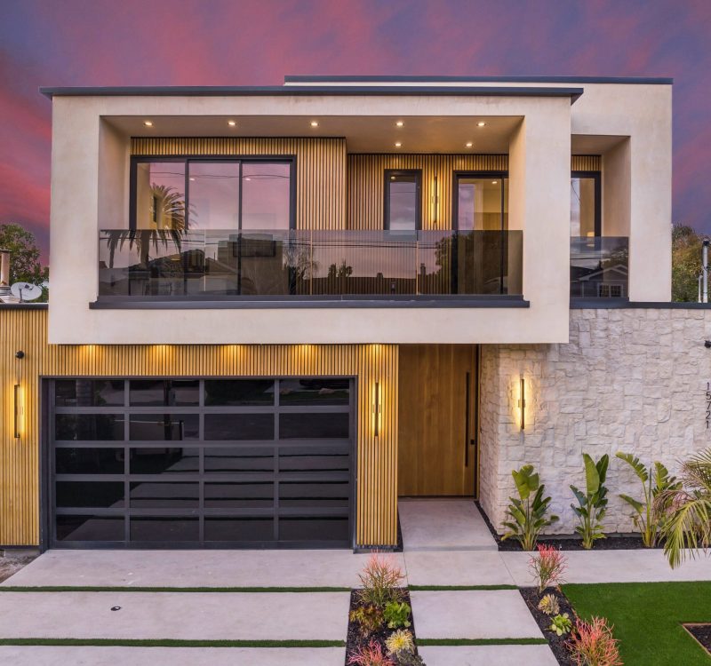 Modern two-story house with large windows and a landscaped front yard at sunset.