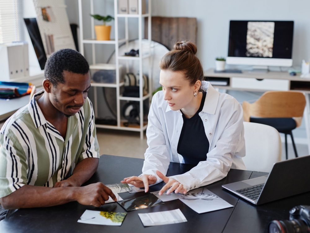 Portrait of two young photographers discussing printed images while working together in studio
